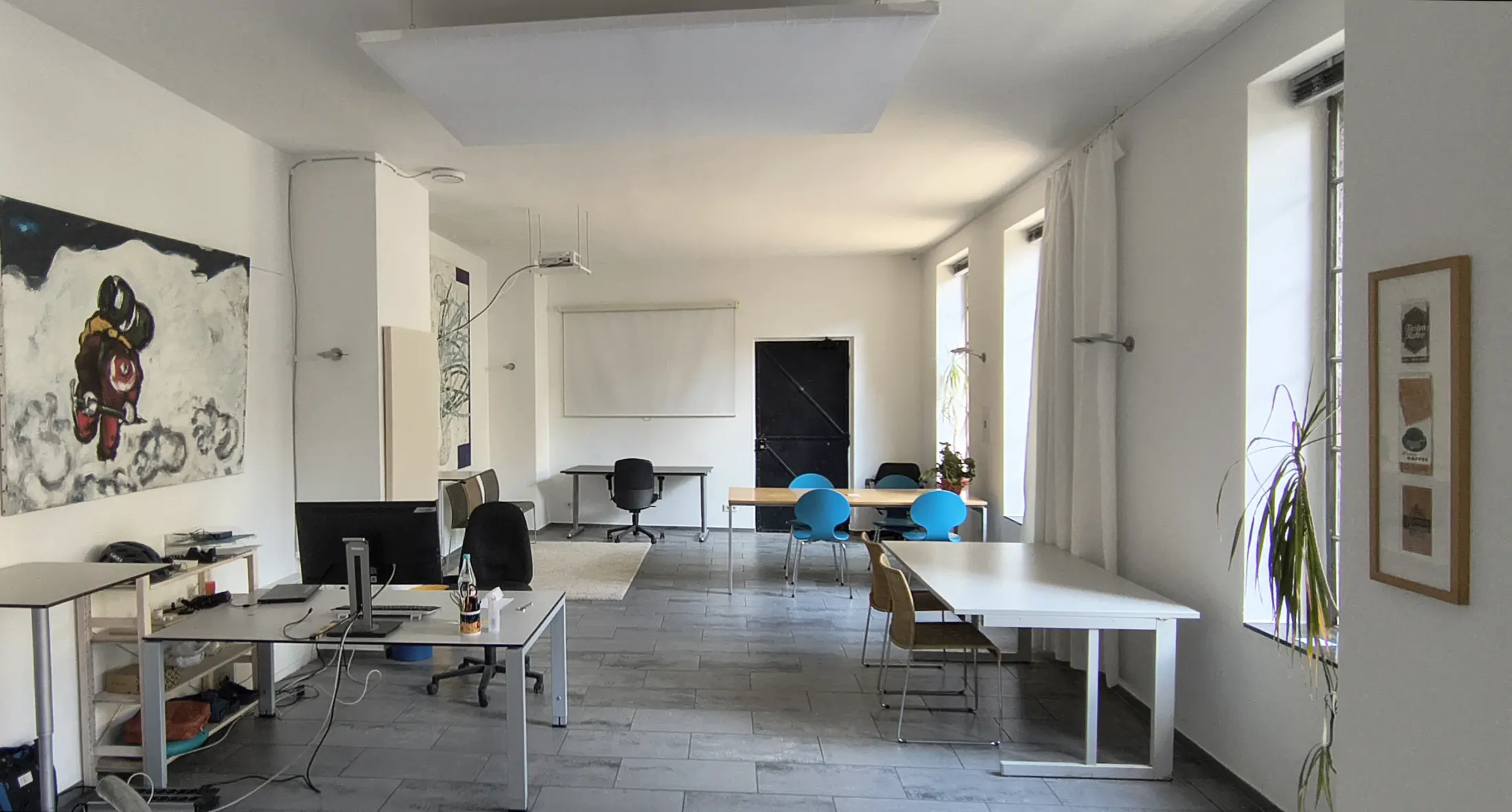 Blick in den Raum mit Schreibtischen, Wandbild und großen Fenstern