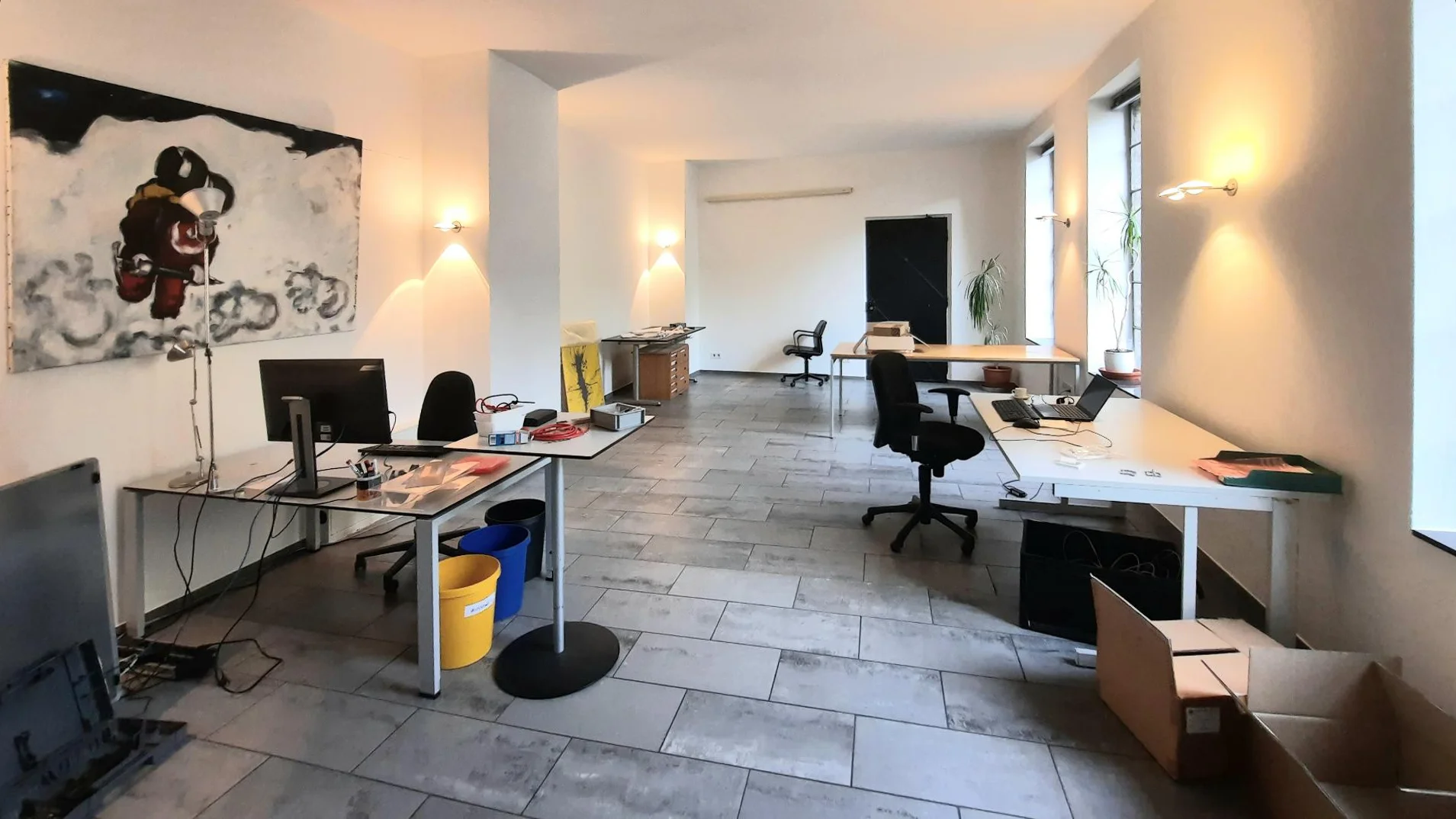 Blick in den Raum mit Schreibtischen, Wandbild und großen Fenstern