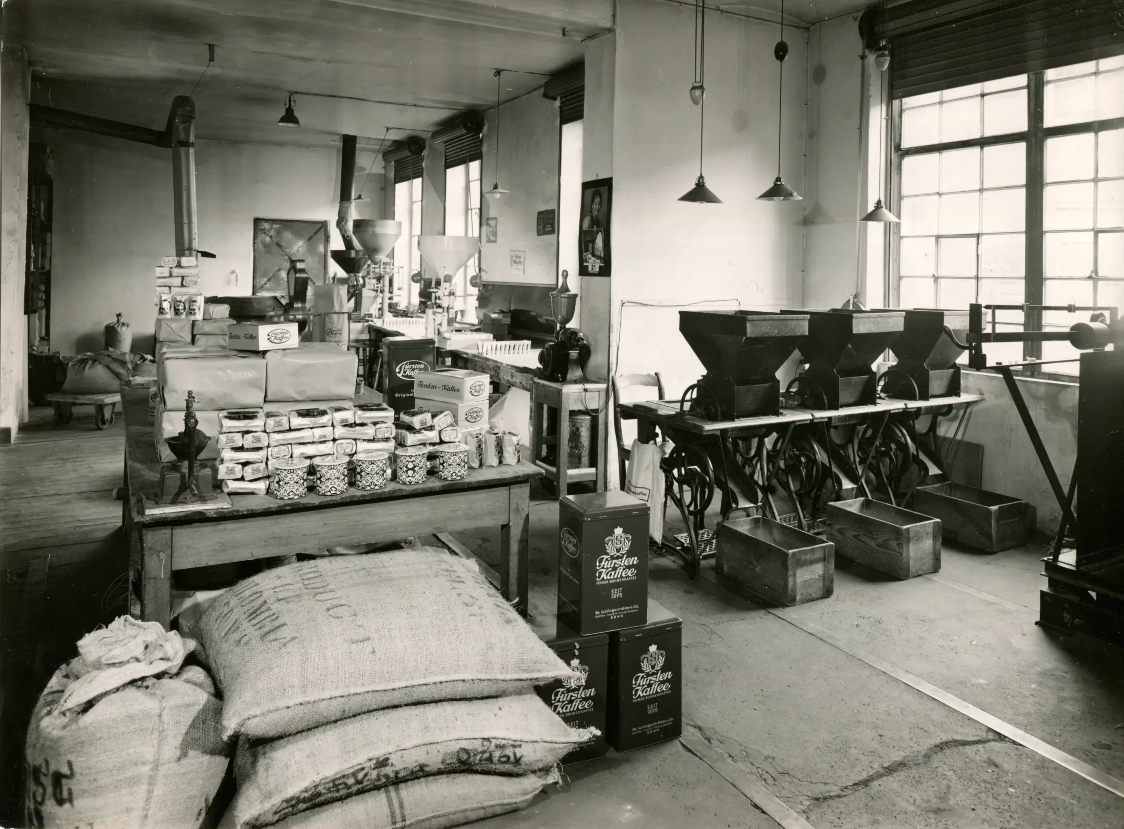 Innenansicht der historischen Rösterei: Kaffeesäcke, Verpackungen und Abfüllmaschinen vor großen Sprossenfenstern